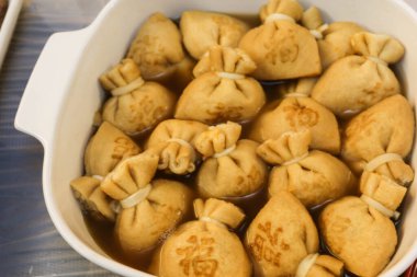 Büyük bir kap haşlanmış Japon tofu (soya peyniri) kesesine yakın pirinç keki (mochi kinchaku) ve Japonca bir kelime olan 