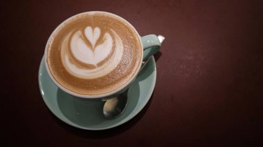 Düz beyaz bir kahvenin üzerinde mavi bir fincanda çiçekli kahve resmi ve fotokopi alanı olan koyu kahverengi bir arka plan.