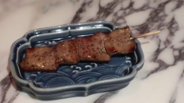 Japon usulü ızgara sığır dili şiş, mavi bir tabakla.