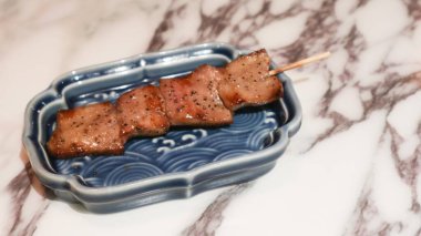 Izakaya restoranındaki mermer bir masada mavi bir tabakta beş parça halinde ızgara öküz dili şişi.
