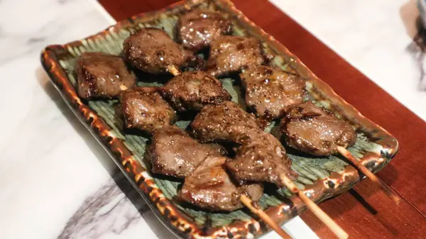 Izakaya restoranında bir tabakta üç şişe ızgara tavuk taşağı yakın. 