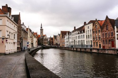 Bruges, Belçika, Avrupa - 15 Mar 2016: Bulutlu bir günde ve taş köprüsü olan kanal boyunca eski gotik renkli misafir evleri