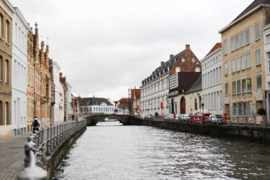 Bruges, Belçika, Avrupa - 15 Mar 2016: Bulutlu bir günde ve taş köprüsü olan kanal boyunca eski gotik renkli misafir evleri