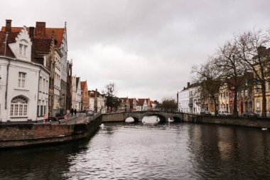 Bruges, Belçika, Avrupa - 15 Mar 2016: Bulutlu bir günde ve taş köprüsü olan kanal boyunca eski gotik renkli misafir evleri