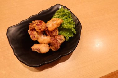 Japon küçük kızartılmış kalamar parçalarını fotokopi alanı olan siyah bir tabakta kapatıyoruz.