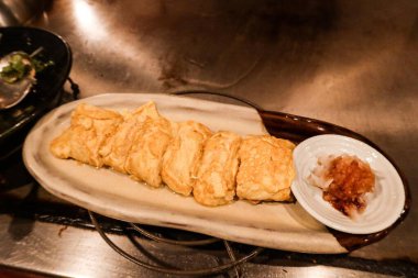 Japon omlet rulolarını (Tamagoyaki) kenarlarında sos olan beyaz bir tabakta parçalara ayırın.
