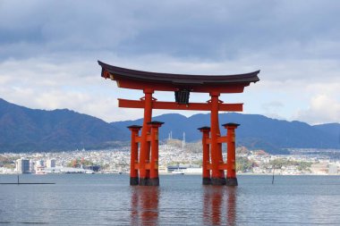 Itsukushima Jinja, Miyajimacho, Hatsukaichi, Hiroşima, Japonya - 9 Aralık 2024: Bulutlu bir günde denizdeki kırmızı torii kapısı yansıma ve kopyalama uzayı