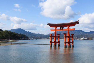 Itsukushima Jinja, Miyajimacho, Hatsukaichi, Hiroşima, Japonya - 9 Aralık 2024: Mavi gökyüzü gününde denizdeki kırmızı torii kapısı yansıması ve kopyasıyla uzay