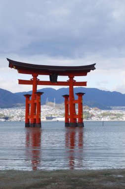 Itsukushima Jinja, Miyajimacho, Hatsukaichi, Hiroşima, Japonya - 9 Aralık 2024: Bulutlu bir günde denizdeki kırmızı torii kapısı yansıma ve kopyalama uzayı