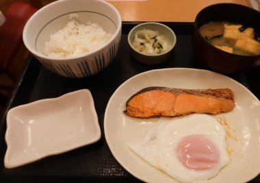 Japon usulü kahvaltıda ızgara somon ve tavada kızartılmış güneşte yumurta, bir kase pilav ve miso çorbası.