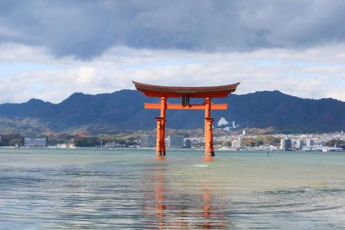 Itsukushima Tapınağı, Miyajimacho, Hatsukaichi, Hiroshima - 8 Aralık 2024: Bulutlu bir günde deniz kenarında yüzen kırmızı torii kapısı 