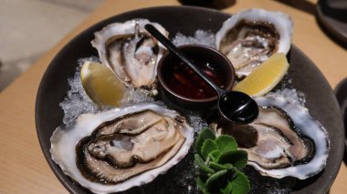 Dört parça taze çiğ istiridyeyi sirke ve limon dilimiyle kaplayıp büyük bir tabakta fotokopi alanına koyun.