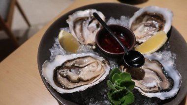 Dört parça taze çiğ istiridyeyi sirke ve limon dilimiyle kaplayıp büyük bir tabakta fotokopi alanına koyun.