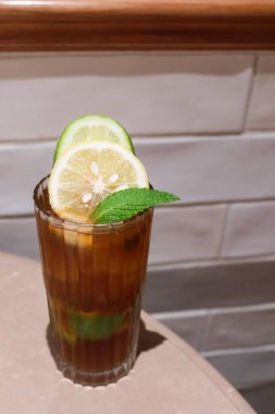 Limon dilimli buzlu limon çayı ve beyaz kiremit duvarlı bir masanın üzerine bir yaprak.