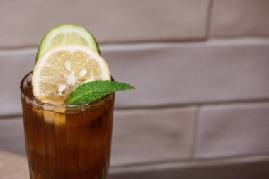 Limon dilimli buzlu limon çayı ve beyaz kiremit duvarlı bir masanın üzerine yerleştirilmiş yaprağın yakın plan fotoğrafı.