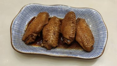 Dört Tayvan usulü soya soslu tavuk kanadını mavi ve beyaz tabakta pişirin.