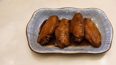 Dört Tayvan usulü soya soslu tavuk kanadını mavi ve beyaz tabakta pişirin.