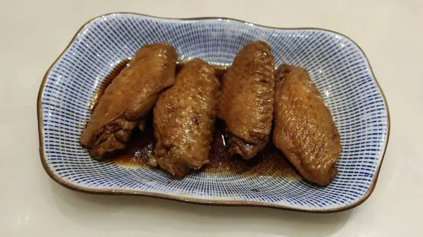 Dört Tayvan usulü soya soslu tavuk kanadını mavi ve beyaz tabakta pişirin.