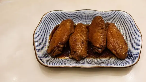 Dört Tayvan usulü soya soslu tavuk kanadını mavi ve beyaz tabakta pişirin.