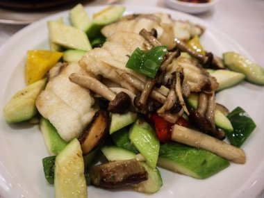 Kanton usulü kızarmış mantar, yeşil biber, orfoz balığı ve beyaz tabakta kabak.