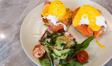 İki parça Benedict yumurtasının yanına hollandaise sosu ve tütsülenmiş somon sosu, yanında da salata.