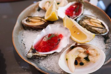 Buz yatağında servis edilen güzel bir tabak taze istiridye. Her istiridyenin üzerinde canlı kırmızı bir jöle ve limon dilimleri ile süslenmiş otlar var.