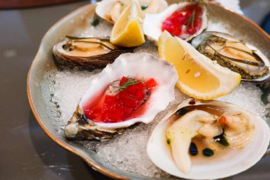 Buz yatağında servis edilen güzel bir tabak taze istiridye. Her istiridyenin üzerinde canlı kırmızı bir jöle ve limon dilimleri ile süslenmiş otlar var.