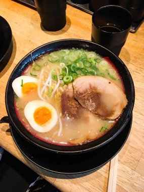 Japon çorbası ramen (domuz dilimi, haşlanmış yumurta, taze soğan) ve yanında ahşap çubuklarla süslenmiş dikey bir fotoğraf.