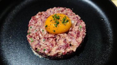 Çiğ yumurta ve ton balıklı tartarı siyah bir tabakta yuvarlak bir şekle sokun.