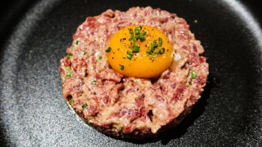 Çiğ yumurta ve ton balıklı tartarı siyah bir tabakta yuvarlak bir şekle sokun.