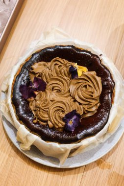 Taze ev yapımı Bask peynirli kekin dikey fotoğrafı. Üstünde Earl Grey çay kreması var. Çiçek de bir kağıt parçasıyla sarılmış.