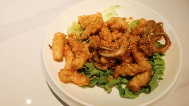 Kanton usulü bol yağda kızartılmış tuz ve biberli kalamarı beyaz tabakta sarımsak ile yakın.