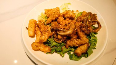 Kanton usulü bol yağda kızartılmış tuz ve biberli kalamarı beyaz tabakta sarımsak ile yakın.