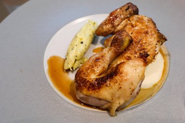 Bir porsiyon kızarmış tavuk, dışı altın ve çıtır çıtır, yanında pürüzsüz, kremalı patates püresi ve beyaz ve gri bir tabak üzerine serpiştirilmiş lezzetli bir sos.