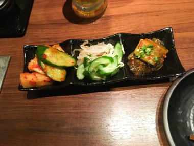 Üç ayrı bölümden oluşan pişirilmemiş başlangıç yemeği, baharatlı salatalık turşusu, terbiye edilmiş patlıcan ve taze fasulye filizi salatası.