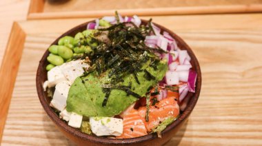 Avokado, tofu, somon, Edamame, kırmızı soğan ve lahana dilimlenmiş Hawaii poke kasesini kapatın. Tahta bir tepside, ahşap bir kasenin üstündeki yosun gibi.