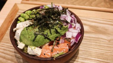 Avokado, tofu, somon, Edamame, kırmızı soğan ve lahana dilimlenmiş Hawaii poke kasesini kapatın. Tahta bir tepside, ahşap bir kasenin üstündeki yosun gibi.