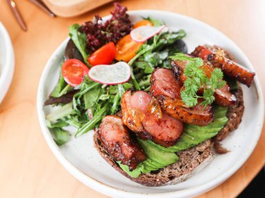 Avokado dilimli ekşi ekmek ve yuzu soslu ördek göğsü. Salata ve vişneli domates beyaz bir tabakta. 