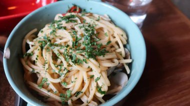 Spagetti alle vongole 'u kapayın, deniz tarakları ve otlarla dolu açık mavi bir tabakta, ahşap bir masada, fotokopi alanı ile.