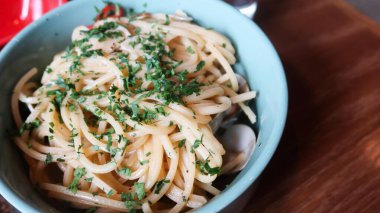 Spagetti alle vongole 'u kapayın, deniz tarakları ve otlarla dolu açık mavi bir tabakta, ahşap bir masada, fotokopi alanı ile.
