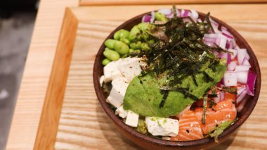 Avokado, tofu, somon, Edamame, kırmızı soğan ve lahana dilimlenmiş Hawaii poke kasesini kapatın. Tahta kasenin üstündeki yosun gibi tahta tepside fotokopi alanı var.