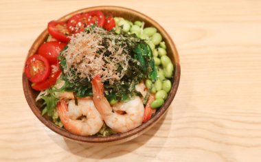 Çiğ karides, vişneli domates, bonito taneleri, edamame, yosunlar ve malzemeler ahşap bir kasede servis edilirken ve üzerinde fotokopi alanı olan tahta bir masada servis edilirken...