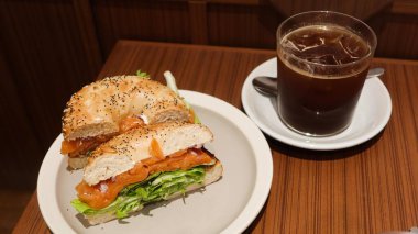 Deniz kabağı tohumlarının yarısının yüzeyi kapanıyor. Somon soslu simit, yanında buzlu, siyah kahve.