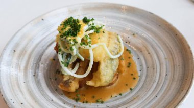 Kızarmış balık filetosunu soğan turşusuyla kaplayın, soğanla süsleyin ve lezzetli bir sosla servis edin, sade gri bir tabakta fotokopi alanı ile sunun.