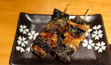 Japon ızgara yılan balığı parçalarını fotokopi alanı olan siyah bir tabakta Kushiyaki 'ye yaklaştır.