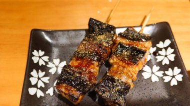 Japon ızgara yılan balığı parçalarını fotokopi alanı olan siyah bir tabakta Kushiyaki 'ye yaklaştır.