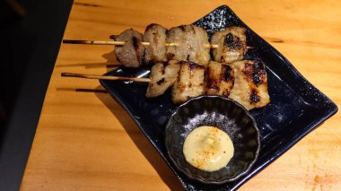 Izgarada iki Japon domuz budu et parçalanmış halde mayonez sosisi ve siyah bir tabakta fotokopi alanı olan küçük bir daldırma kabıyla.