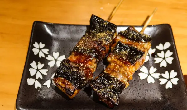 Japon ızgara yılan balığı parçalarını fotokopi alanı olan siyah bir tabakta Kushiyaki 'ye yaklaştır.