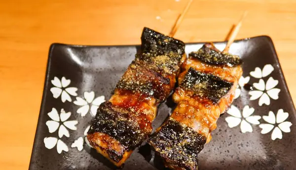 Japon ızgara yılan balığı parçalarını fotokopi alanı olan siyah bir tabakta Kushiyaki 'ye yaklaştır.