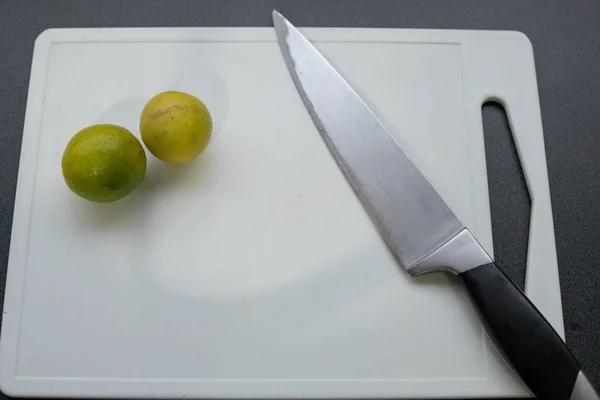 Two limes and a knife on a cutting board with a dark background viewed from above
